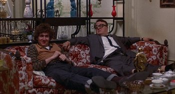 Movie still from “Little Murders” (1971), directed by Alan Arkin – Two men are sitting on a couch and one of them is holding a video game controller; Medium shot, Low angle