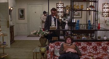 Movie still from “Little Murders” (1971), directed by Alan Arkin – A man sitting on top of a couch in a living room; Wide shot, High angle