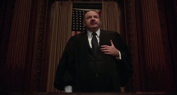 Movie still from “Little Murders” (1971), directed by Alan Arkin – A man in a black robe stands in front of an american flag; Medium shot, Low angle
