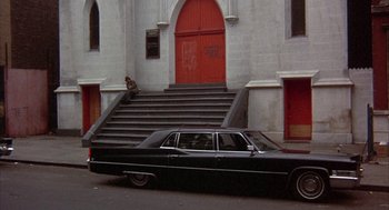 Movie still from “Little Murders” (1971), directed by Alan Arkin – A black car parked in front of a building; Wide shot, High angle
