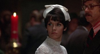 Movie still from “Little Murders” (1971), directed by Alan Arkin – A woman in a white dress with a bow on top of her head; Close Up shot, Low angle