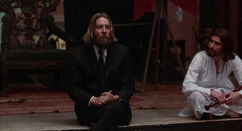 Movie still from “Little Murders” (1971), directed by Alan Arkin – A man sitting on the ground wearing a suit and tie; Medium shot, Low angle