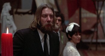 Movie still from “Little Murders” (1971), directed by Alan Arkin – A man with long hair and a beard standing next to two other people; Close Up shot, Low angle