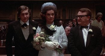 Movie still from “Little Murders” (1971), directed by Alan Arkin – A woman holding a bouquet of flowers in front of a crowd; Medium shot, Over the shoulder angle