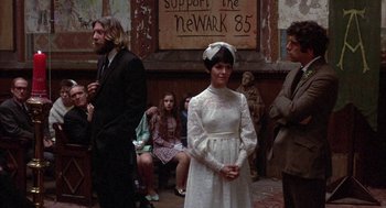 Movie still from “Little Murders” (1971), directed by Alan Arkin – A woman in a white dress standing in front of a crowd; Medium shot, Low angle