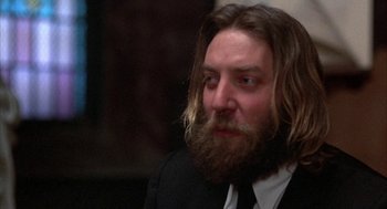 Movie still from “Little Murders” (1971), directed by Alan Arkin – A man with long hair and a long beard wearing a suit and tie; Close Up shot, Low angle