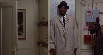 Movie still from “Little Murders” (1971), directed by Alan Arkin – A man wearing a hat and a trench coat standing in front of a door; Medium shot, Low angle