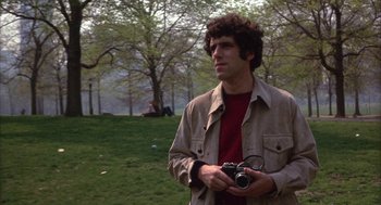 Movie still from “Little Murders” (1971), directed by Alan Arkin – A man holding a camera in a park; Medium shot, Low angle