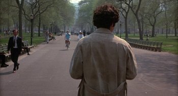 Movie still from “Little Murders” (1971), directed by Alan Arkin – A man is walking down the street while people are riding bikes; Wide shot, Over the shoulder angle