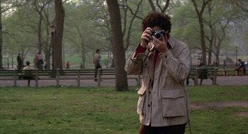 Movie still from “Little Murders” (1971), directed by Alan Arkin – A man taking a picture in a park with a camera; Medium shot, Over the shoulder angle