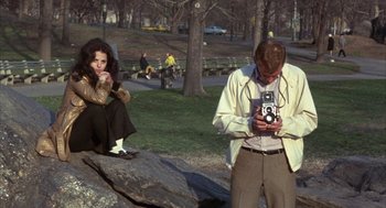 Movie still from “Little Murders” (1971), directed by Alan Arkin – A man holding a camera while sitting next to a woman; Wide shot, High angle