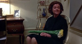 Movie still from “Little Murders” (1971), directed by Alan Arkin – A woman sitting in a chair holding a bouquet of flowers; Medium shot, Over the shoulder angle