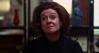 Movie still from “Little Murders” (1971), directed by Alan Arkin – An older woman sitting in a chair looking at the camera; Close Up shot, Over the shoulder angle