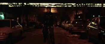 Movie still from “Little Odessa” (1994), directed by James Gray – A person riding a bike on a street at night; Wide shot, Low angle