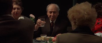 Movie still from “Little Odessa” (1994), directed by James Gray – An old man sitting at a dinner table holding a glass of water; Medium shot, Over the shoulder angle