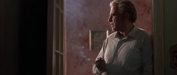 Movie still from “Little Odessa” (1994), directed by James Gray – An older man standing in front of a window with smoke coming out of his mouth; Medium shot, Low angle