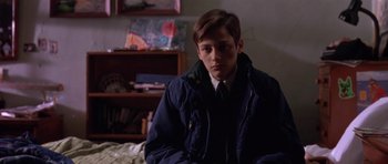 Movie still from “Little Odessa” (1994), directed by James Gray – A young man sitting on a bed wearing a jacket; Medium shot, Low angle