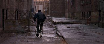 Movie still from “Little Odessa” (1994), directed by James Gray – A person riding a bike down a street; Wide shot, High angle