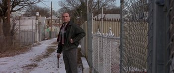 Movie still from “Little Odessa” (1994), directed by James Gray – A man holding a gun standing next to a fence; Medium shot, Low angle