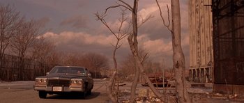 Movie still from “Little Odessa” (1994), directed by James Gray – A car parked on the side of the road next to trees; Extreme Wide shot, Low angle