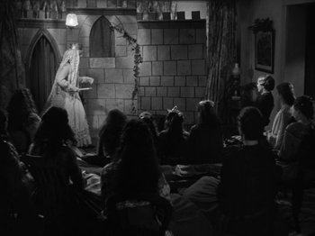 Movie still from “Little Women” (1933), directed by George Cukor – A group of people sitting in a room with a woman in a white dress; Wide shot, High angle