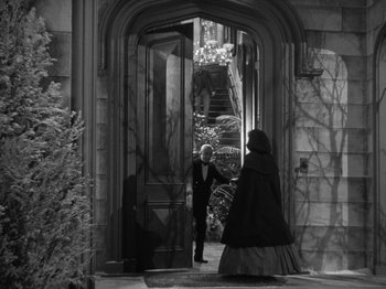 Movie still from “Little Women” (1933), directed by George Cukor – A man and a woman are standing in front of an open door; Wide shot, High angle