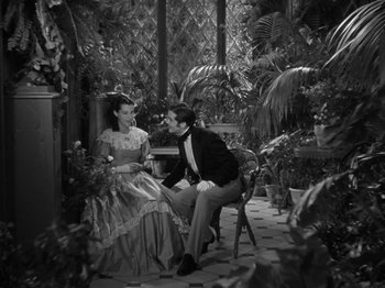 Movie still from “Little Women” (1933), directed by George Cukor – A man and a woman sitting on a chair in a room filled with plants; Medium shot, High angle