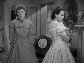 Movie still from “Little Women” (1933), directed by George Cukor – Two women in vintage dresses standing next to each other in a living room; Medium shot, Low angle