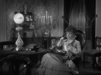 Movie still from “Little Women” (1933), directed by George Cukor – A woman sitting in a chair in front of a lamp; Medium shot, High angle