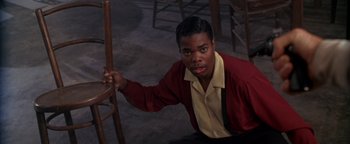 Movie still from “Lone Star” (1996), directed by John Sayles – A man in a red jacket holding a wooden chair; Medium shot, High angle
