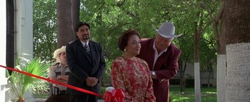 Movie still from “Lone Star” (1996), directed by John Sayles – An older man cutting a red ribbon for a woman in a red dress; Medium shot, High angle