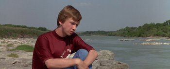 Movie still from “Lone Star” (1996), directed by John Sayles – A young man sitting on the ground near a body of water; Close Up shot, Low angle