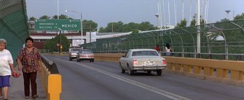 Movie still from “Lone Star” (1996), directed by John Sayles – Cars driving down a street near a bridge; Extreme Wide shot, Over the shoulder angle