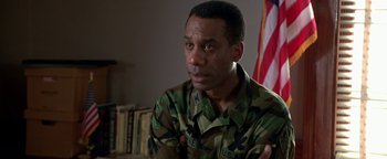 Movie still from “Lone Star” (1996), directed by John Sayles – A man in military fatigues sitting in front of an american flag; Close Up shot, High angle