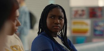 Movie still from “Everything Now” (2023), created by Ripley Parker – A young woman with long black hair wearing a blue shirt; Close Up shot, Over the shoulder angle