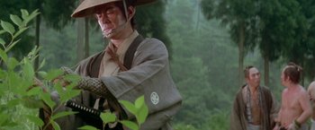 Movie still from “Lone Wolf and Cub: Baby Cart to Hades” (1972), directed by Kenji Misumi – A man in a hat and a jacket holding an umbrella over his head; Close Up shot, Low angle