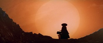 Movie still from “Lone Wolf and Cub: Baby Cart to Hades” (1972), directed by Kenji Misumi – A person standing on top of a hill with a suitcase; Extreme Wide shot, Low angle