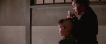 Movie still from “Lone Wolf and Cub: Baby Cart to Hades” (1972), directed by Kenji Misumi – A young boy getting his hair cut by an adult; Close Up shot, Over the shoulder angle
