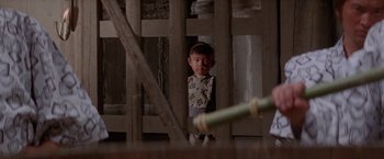 Movie still from “Lone Wolf and Cub: Baby Cart to Hades” (1972), directed by Kenji Misumi – A young boy standing in front of a wooden fence; Medium shot, Low angle