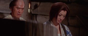 Movie still from “Lone Wolf and Cub: Baby Cart to Hades” (1972), directed by Kenji Misumi – A woman sitting in front of a wooden wall; Medium shot, Low angle