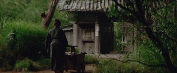 Movie still from “Lone Wolf and Cub: Baby Cart to Hades” (1972), directed by Kenji Misumi – A woman pushing a wheelbarrow in front of a house; Wide shot, High angle