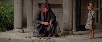 Movie still from “Lone Wolf and Cub: Baby Cart to Hades” (1972), directed by Kenji Misumi – A man in a robe is kneeling on the ground and looking at a cell phone; Medium shot, Low angle