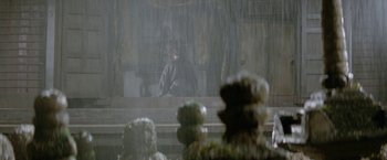 Movie still from “Lone Wolf and Cub: Baby Cart to Hades” (1972), directed by Kenji Misumi – A man sitting on a bench in the pouring rain; Wide shot, Over the shoulder angle