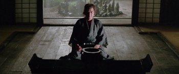 Movie still from “Lone Wolf and Cub: Baby Cart to Hades” (1972), directed by Kenji Misumi – A person sitting on the ground holding a bowl; Wide shot, Low angle