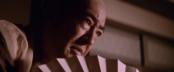 Movie still from “Lone Wolf and Cub: Baby Cart to Hades” (1972), directed by Kenji Misumi – An older man holding a fan in front of his face; Close Up shot, Low angle