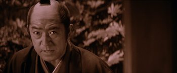 Movie still from “Lone Wolf and Cub: Baby Cart to Hades” (1972), directed by Kenji Misumi – An older man with a bald head in front of some trees; Close Up shot, Low angle