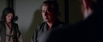 Movie still from “Lone Wolf and Cub: Baby Cart to Hades” (1972), directed by Kenji Misumi – A man in a black shirt is looking down; Close Up shot, Over the shoulder angle