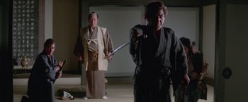 Movie still from “Lone Wolf and Cub: Baby Cart to Hades” (1972), directed by Kenji Misumi – A man and a woman holding a sword in front of a wall; Medium shot, Low angle