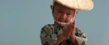 Movie still from “Lone Wolf and Cub: Baby Cart to Hades” (1972), directed by Kenji Misumi – A little boy wearing a straw hat and holding his hands up; Close Up shot, Low angle