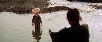 Movie still from “Lone Wolf and Cub: Baby Cart to Hades” (1972), directed by Kenji Misumi – A child in the middle of a body of water with an umbrella on his head; Wide shot, High angle